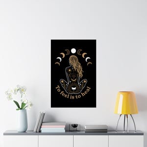 May include: Black poster featuring a seated figure with long, wavy hair, adorned with celestial body designs. The artwork includes a crescent moon and sun motif, with the text "To feel is to heal" in a circular arrangement.