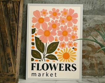 May include: A framed art print featuring a floral design with pink and yellow flowers, green leaves, and the words "FLOWERS market" in black. A potted aloe vera plant in a woven basket and a wooden crate are also visible.