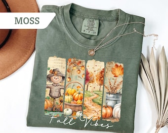 May include: Moss green Comfort Colors t-shirt with a fall-themed graphic. The graphic features a scarecrow, pumpkins, and autumn foliage. The words "Fall Vibes" are written in a script font across the bottom of the graphic.