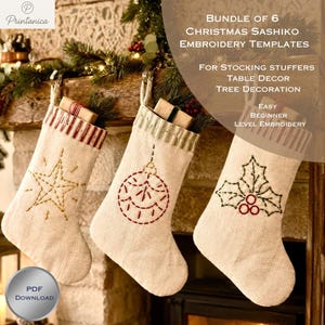 Puede incluir: Tres calcetines navideños de lino beige con diseños bordados a mano. El calcetín izquierdo muestra una estrella amarilla, el central un adorno rojo y el derecho una hoja de acebo verde. Cada uno tiene un puño a rayas y un lazo para colgar.