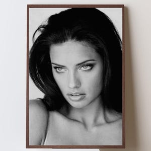 Puede incluir: Retrato enmarcado en blanco y negro de una mujer con cabello largo y oscuro. El retrato es un primer plano del rostro de la mujer, con un enfoque suave y una expresión contemplativa. El marco es de color marrón oscuro.