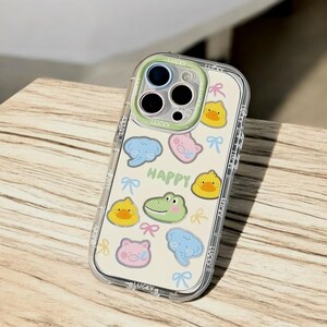 May include: A clear phone case with a white background and colorful cartoon animal stickers. The case has a cutout for the camera lens and the word "HAPPY" is printed on the case.
