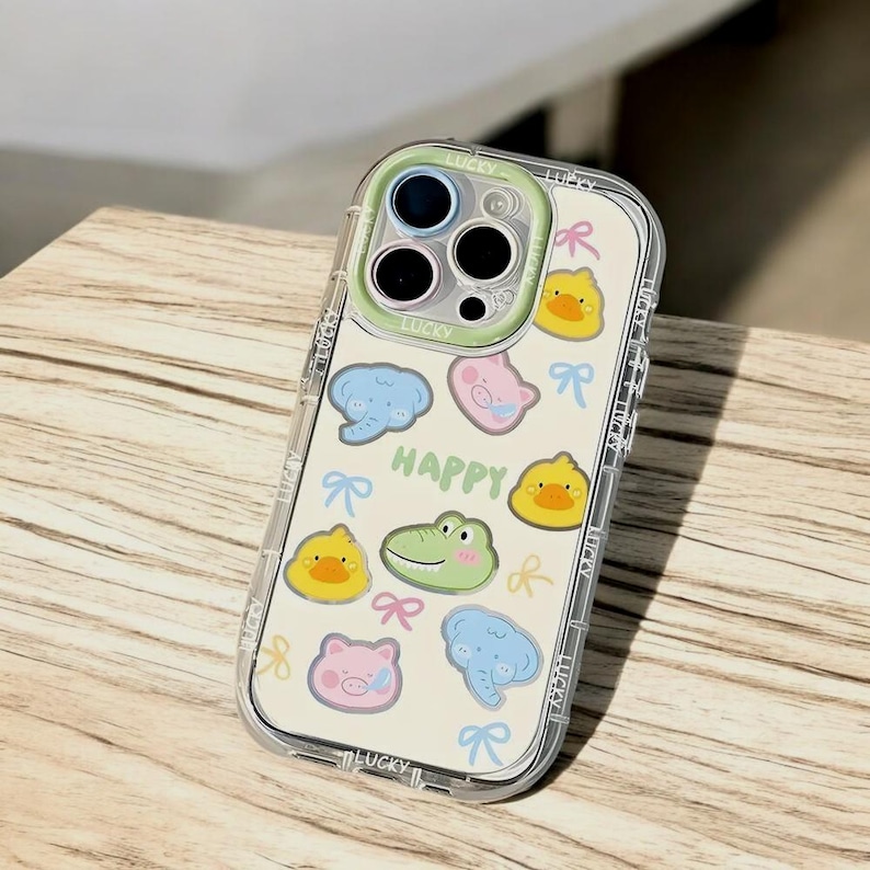 May include: A clear phone case with a white background and colorful cartoon animal stickers. The case has a cutout for the camera lens and the word "HAPPY" is printed on the case.