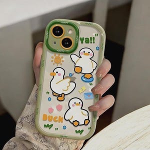 May include: A clear phone case with a green border and a cartoon duck design. The case has the words "Happy" and "Duck" printed on it. The case also has a cartoon sun, a cartoon envelope, and a cartoon heart.