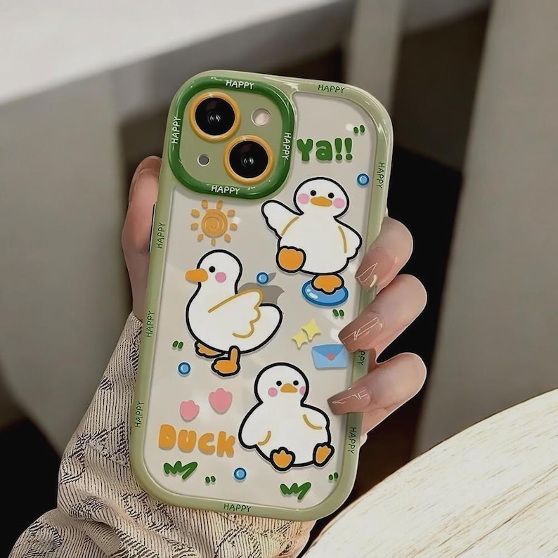 May include: A clear phone case with a green border and a cartoon duck design. The case has the words "Happy" and "Duck" printed on it. The case also has a cartoon sun, a cartoon envelope, and a cartoon heart.