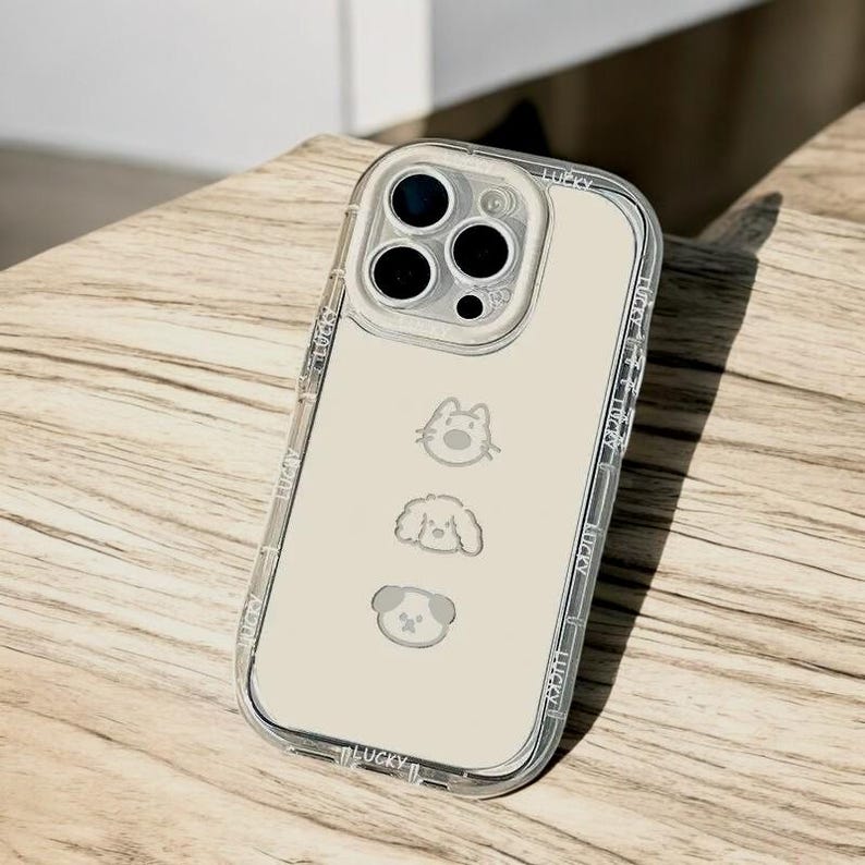 May include: A clear phone case with a white background and a design of three animals: a cat, a dog, and a puppy. The case has a raised edge around the camera lens and the word "LUCKY" printed on the bottom.