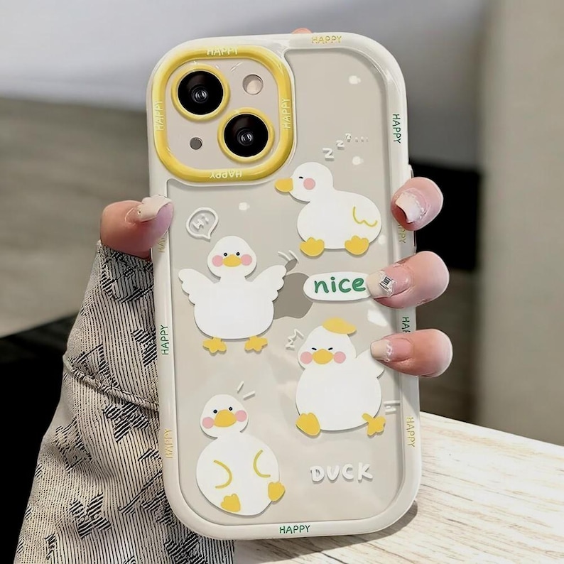 May include: A clear phone case with a yellow border and a cutout for the camera. The case has a cartoon design of ducks with the words "Happy", "Nice", and "Duck" printed on it.