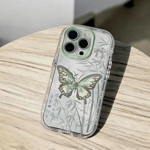 May include: A clear phone case with a green butterfly and bamboo design. The case has a raised camera ring with the word "Lucky" printed on it.