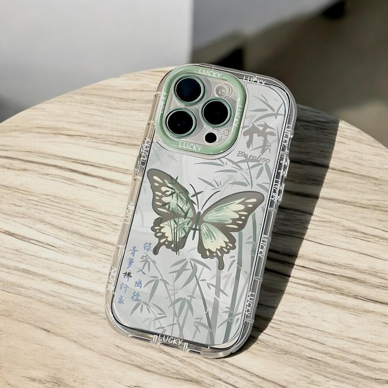 May include: A clear phone case with a green butterfly and bamboo design. The case has a raised camera ring with the word "Lucky" printed on it.