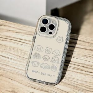 May include: A clear phone case with a beige background and a white outline of various dog breeds. The case has a camera lens cutout with three black circles. The text "Have a good day!" is printed on the bottom of the case.