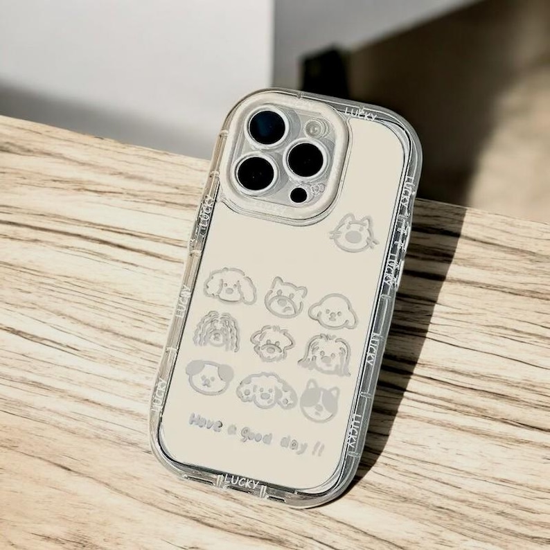 May include: A clear phone case with a beige background and a white outline of various dog breeds. The case has a camera lens cutout with three black circles. The text "Have a good day!" is printed on the bottom of the case.