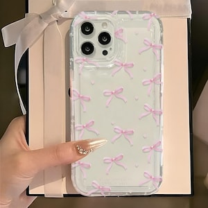 May include: Clear phone case with a pink bow pattern. The case is designed for a phone with a triple lens camera.