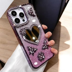 May include: A sparkly purple phone case with a heart-shaped mirror, rhinestones, and butterfly designs.