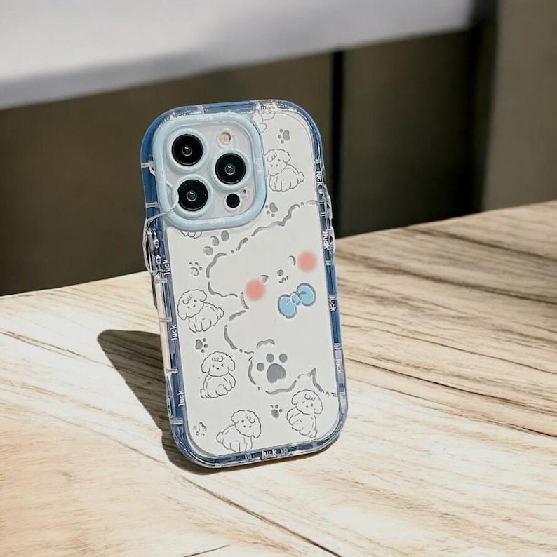 May include: A clear phone case with a white background and a cute cartoon dog design. The case has a blue trim and a cutout for the camera lens.
