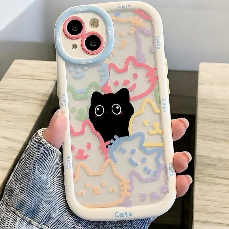 May include: A white phone case with a clear back. The back of the case has a colorful design of cats with the word "Cats" written on the side.