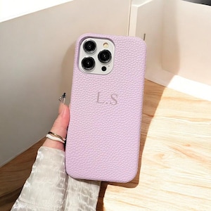 Puede incluir: Una funda de teléfono de cuero lavanda con un relieve de cámara elevado y las iniciales "L.S." grabadas en la parte posterior.