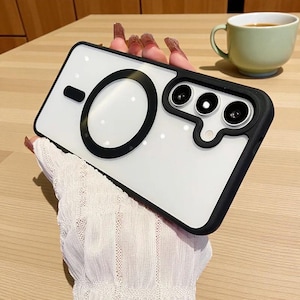 May include: A clear phone case with a black border and a large black circle design. The case has a camera cutout with three lenses. The phone case is held by a person wearing a white lace sleeve.