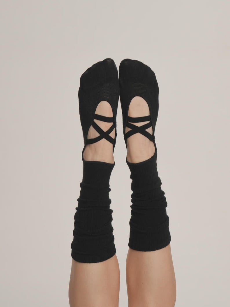 Puede incluir: Calcetines negros estilo ballet con correas entrecruzadas en la parte superior del pie. Los calcetines tienen un dise&ntilde;o recortado y se extienden hasta la parte inferior de la pierna. El fondo es de color neutro s&oacute;lido.