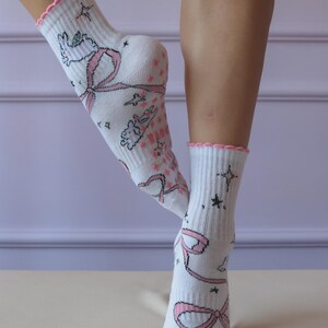 May include: White socks with pink bows, stars, and cartoon characters. The socks have a pink scalloped trim at the top. The socks are knee-high and made of a soft material.