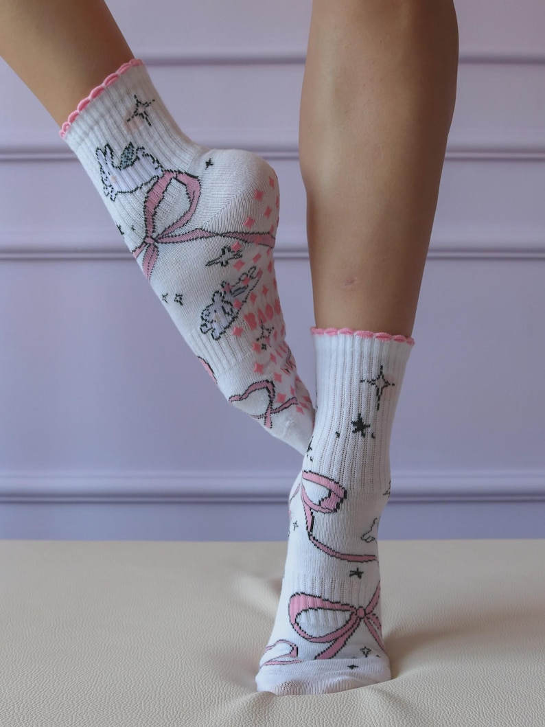 May include: White socks with pink bows, stars, and cartoon characters. The socks have a pink scalloped trim at the top. The socks are knee-high and made of a soft material.