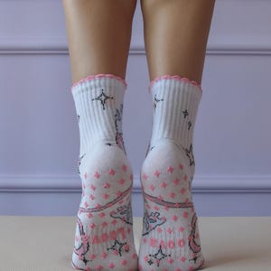 May include: White socks with pink accents and a scalloped edge. The socks feature a pattern of pink diamonds, stars, and floral designs. The socks are ribbed at the top and have a soft, comfortable appearance.