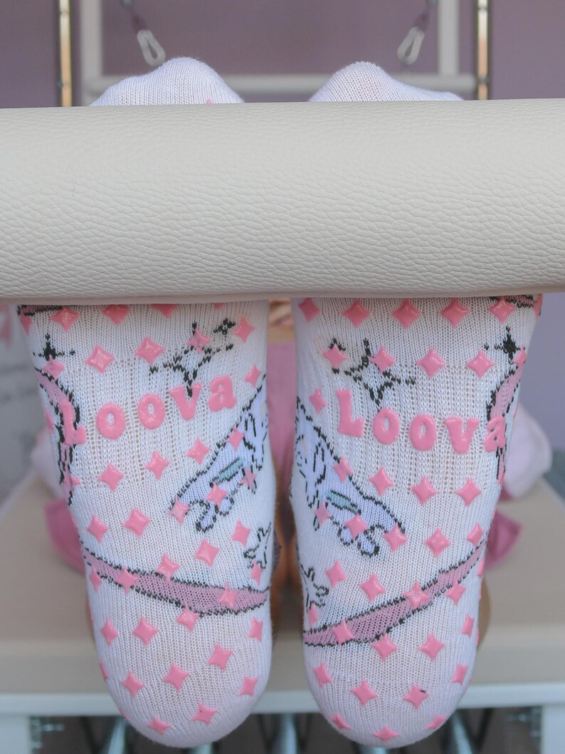 May include: White socks with pink diamond-shaped grips and the word "Loova" printed in pink. The socks feature a pink band and a whimsical design. The socks are designed for comfort and grip.