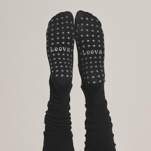 Puede incluir: Calcetines negros con un patr&oacute;n de estrellas y la palabra "Loova" impresa en las suelas. Los calcetines son largos y tienen una textura acanalada. El fondo es de color neutro.