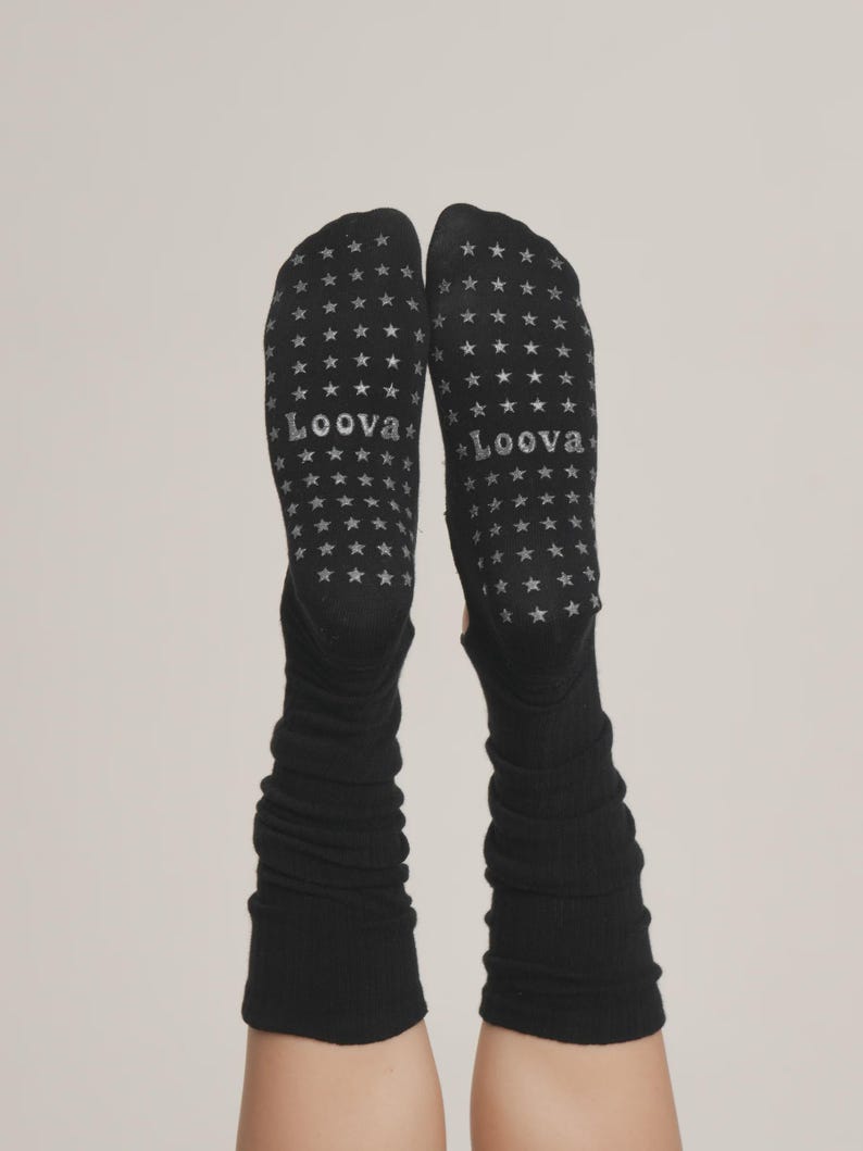 Puede incluir: Calcetines negros con un patr&oacute;n de estrellas y la palabra "Loova" impresa en las suelas. Los calcetines son largos y tienen una textura acanalada. El fondo es de color neutro.