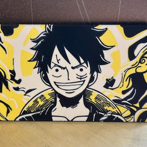 Pode incluir: Uma carteira retangular com uma ilustração a preto e branco de uma personagem com cabelo preto espetado e uma cicatriz sob o olho, num fundo amarelo com padrões rodopiantes. A carteira tem uma borda preta.