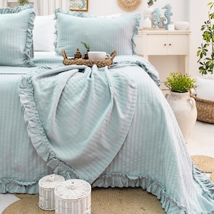May include: A light blue bedspread with a ruffled edge and a waffle-like texture. The bedspread is on a bed with white pillows and a light blue throw pillow.
