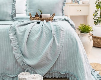 May include: A light blue bedspread with a ruffled edge and a waffle-like texture. The bedspread is on a bed with white pillows and a light blue throw pillow.
