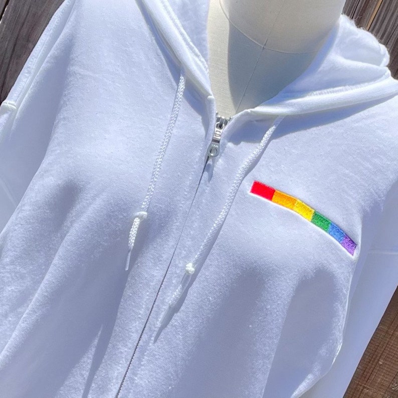 May include: White zippered hoodie with a rainbow embroidered patch on the front.