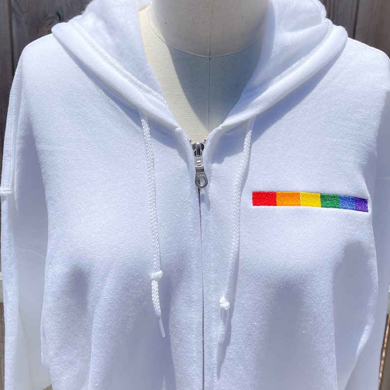 May include: White zippered hoodie with a rainbow embroidered patch on the left chest.