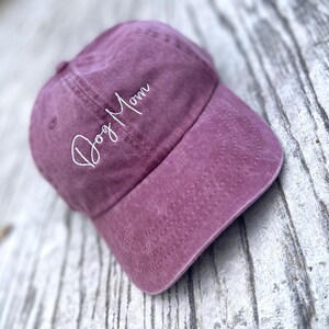 May include: A dusty rose baseball cap with the embroidered text "Dog Mom" in white script. The cap has a curved brim and a classic six-panel design, perfect for casual wear.