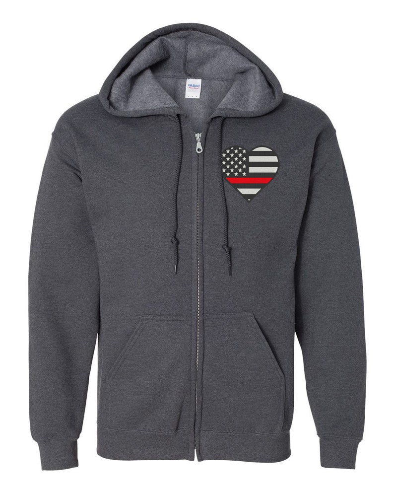 K&ouml;nnte beinhalten: Ein dunkelgrauer Rei&szlig;verschluss-Hoodie mit einem roten Streifen durch eine herzf&ouml;rmige amerikanische Flagge auf der linken Brust.