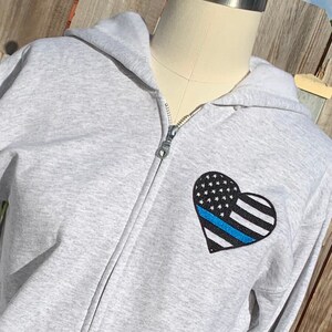 May include: A gray zip-up hoodie with a blue line American flag heart on the front.