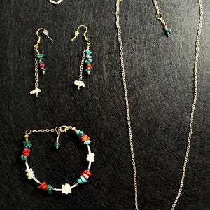 以下が含まれることがあります： ゴールドトーンのジュエリーコレクション。リング、イヤリング、ブレスレット、ネックレスが含まれています。赤、緑、白の石のアクセントが特徴です。イヤリングとネックレスには揺れる要素があり、ブレスレットはチェーンです。