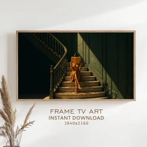 May include: A digital artwork displayed on a television screen featuring a person in a mustard yellow dress sitting on wooden stairs, holding an open book in front of their face. The scene includes a dark green paneled wall and a staircase railing.