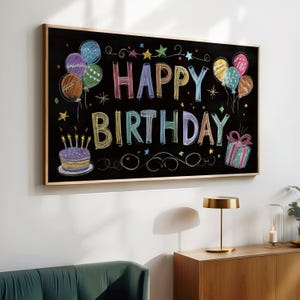 May include: A framed chalkboard with the words "HAPPY BIRTHDAY" in colorful chalk lettering. The board features drawings of balloons, a cake with candles, and a wrapped gift. The frame is a light brown color.