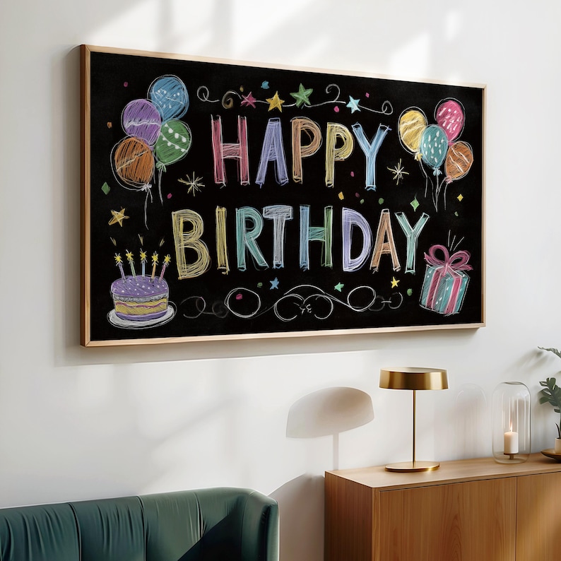May include: A framed chalkboard with the words "HAPPY BIRTHDAY" in colorful chalk lettering. The board features drawings of balloons, a cake with candles, and a wrapped gift. The frame is a light brown color.