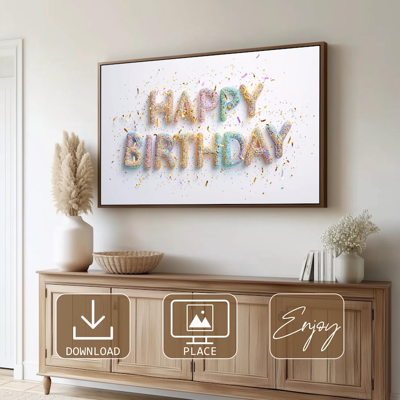 May include: A framed print with the words "HAPPY BIRTHDAY" in colorful, textured letters, sprinkled with confetti. The artwork is displayed above a wooden cabinet with decorative elements, including a vase with pampas grass and a woven bowl.