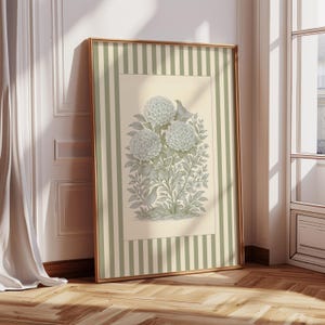 Puede incluir: Una impresión botánica enmarcada que presenta un arreglo floral con tres grandes flores redondas y dos pájaros. La obra de arte está en tonos suaves de verde y gris, sobre un fondo crema con un borde a rayas. El marco es dorado.