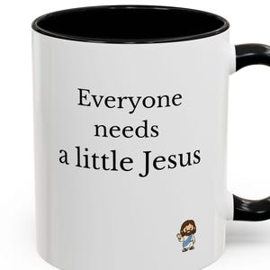 May include: A white ceramic mug with a black interior and a black handle. The exterior features the black text "Everyone needs a little Jesus" printed in a serif font, accompanied by a small, colorful cartoon illustration of Jesus below.