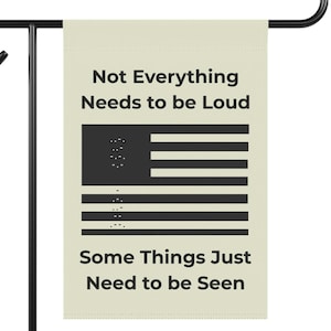 Könnte beinhalten: Eine beige Gartenflagge mit schwarzem Text und einem schwarzen Flaggen-Design. Der Text lautet: "Not Everything Needs to be Loud" und "Some Things Just Need to be Seen". Das Flaggen-Design ähnelt der amerikanischen Flagge, wobei die Sterne durch Braille-Punkte ersetzt wurden.