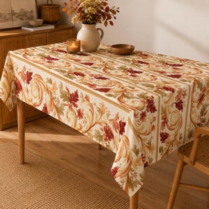 May include: A rectangular tablecloth featuring a repeating pattern of swirling golden scrolls and autumn-colored leaves in shades of deep red, orange, and muted green on a cream-colored background, draped over a wooden table.