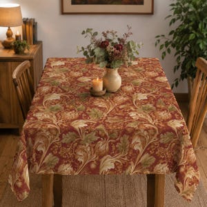 May include: A rectangular tablecloth featuring a deep red background with a repeating pattern of large, light-colored acanthus leaves, foliage, and small acorns in shades of cream, tan, and muted green, covering the entire surface of the table.