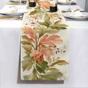 May include: A rectangular table runner featuring a printed pattern of autumn-colored oak leaves, acorns, and small red berries on a cream-colored background. The design displays shades of orange, brown, and muted green foliage.