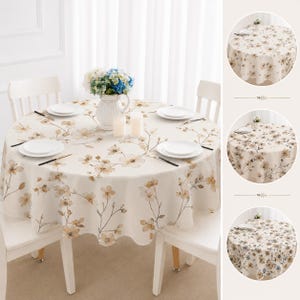 May include: A round tablecloth featuring a cream-colored base with a repeating pattern of delicate brown and tan floral branches. The tablecloth is draped over a circular table set with white plates, a white pitcher, and two white candles.