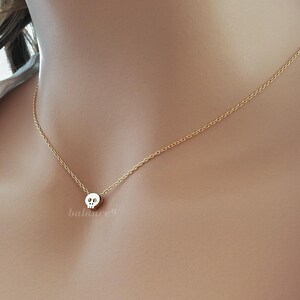 Puede incluir: Un delicado collar dorado con un peque&ntilde;o colgante de calavera. La calavera tiene detalles de ojos y nariz. El collar se muestra en el cuello de una persona, mostrando el tama&ntilde;o y el dise&ntilde;o del colgante. La cadena es fina y elegante.