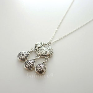 May include: A silver necklace with a charm that resembles a stylised heart with intricate designs. The charm has three dangling charms that are round and have a similar design.